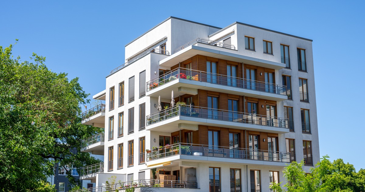 Modern multi-family apartment building exterior with wood-clad balconies against a clear blue sky