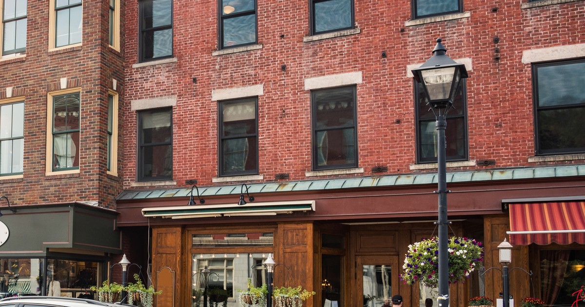 Historic red brick buildings with arched windows above wood-framed storefronts and a black street lamp with hanging flower baskets